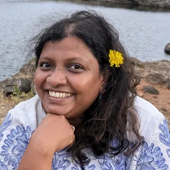 Nivedita Louis, smiling, with a yellow flower in her hair, beside water