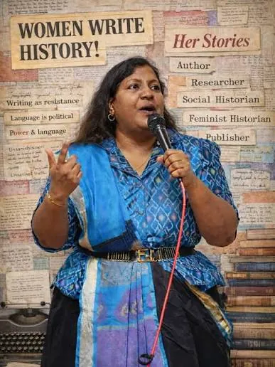 Nivedita Louis speaking into a microphone before a wall reading Women Write History